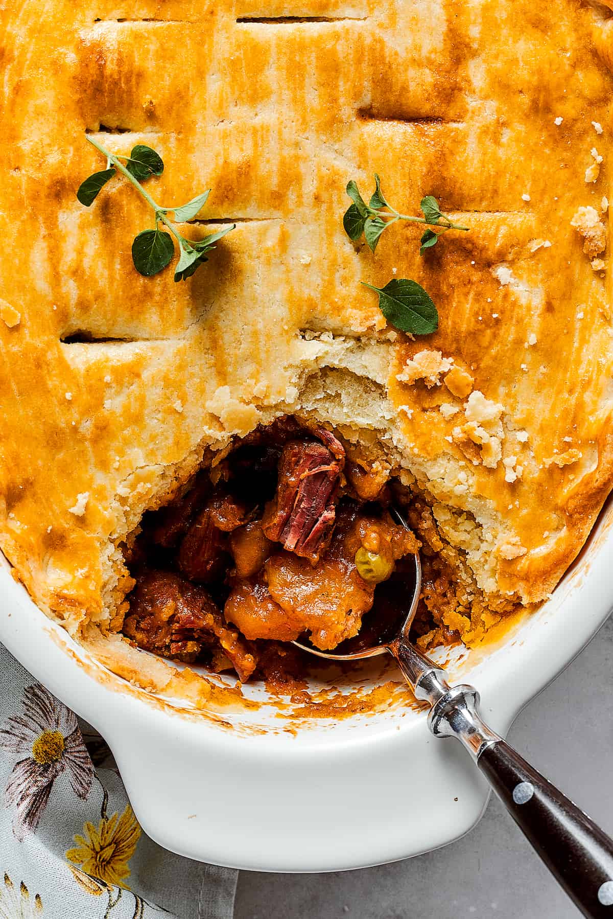 Comforting Beef Pot Pie is packed with tender beef and vegetables tucked into a stout-based gravy with flaky pie crust balanced on top. A beef pot pie is shown in a baking dish with a spoon.