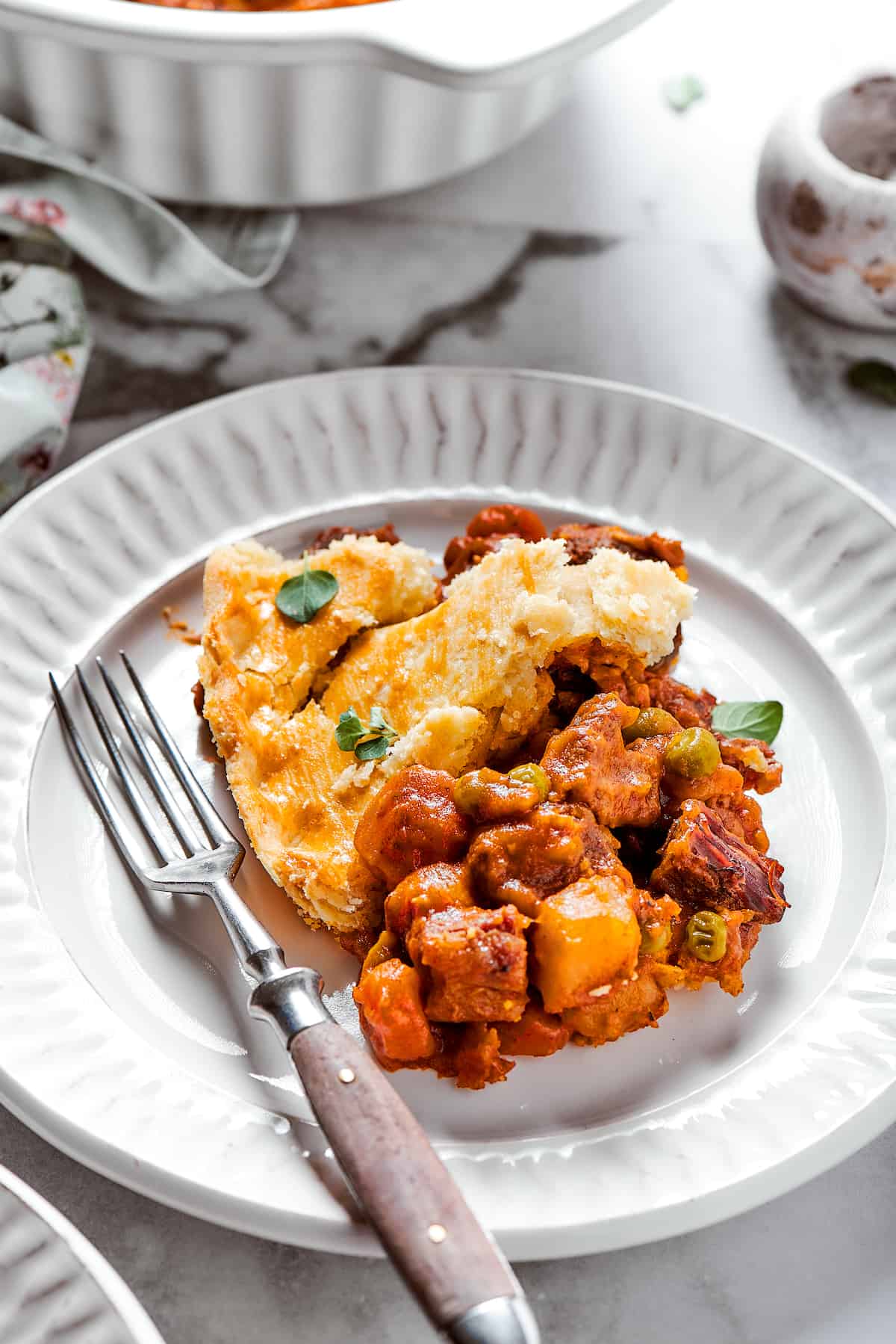 Comforting Beef Pot Pie is packed with tender beef and vegetables tucked into a stout-based gravy with flaky pie crust balanced on top. A white plate of beef pot pie with a fork.