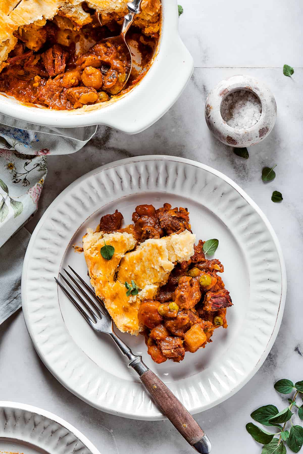 Comforting Beef Pot Pie is packed with tender beef and vegetables tucked into a stout-based gravy with flaky pie crust balanced on top. A plate of beef pot pie is shown with a fork and a dish of pot pie next to it.