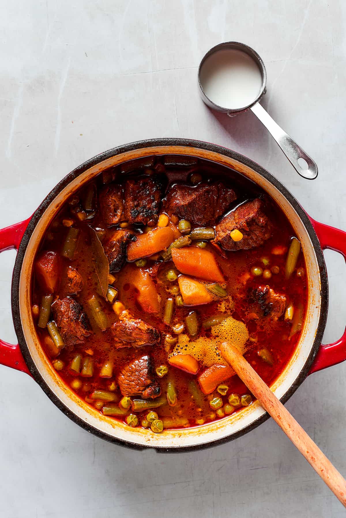 Comforting and rich Beef Pot Pie is packed with tender beef and vegetables tucked into a stout-based gravy with a wonderfully flaky pie crust balanced on top. You can enjoy this hearty meal the day of, or make it in advance and freeze it for dinner another time! A wooden spoon stirs a pot of Mulligan stew.