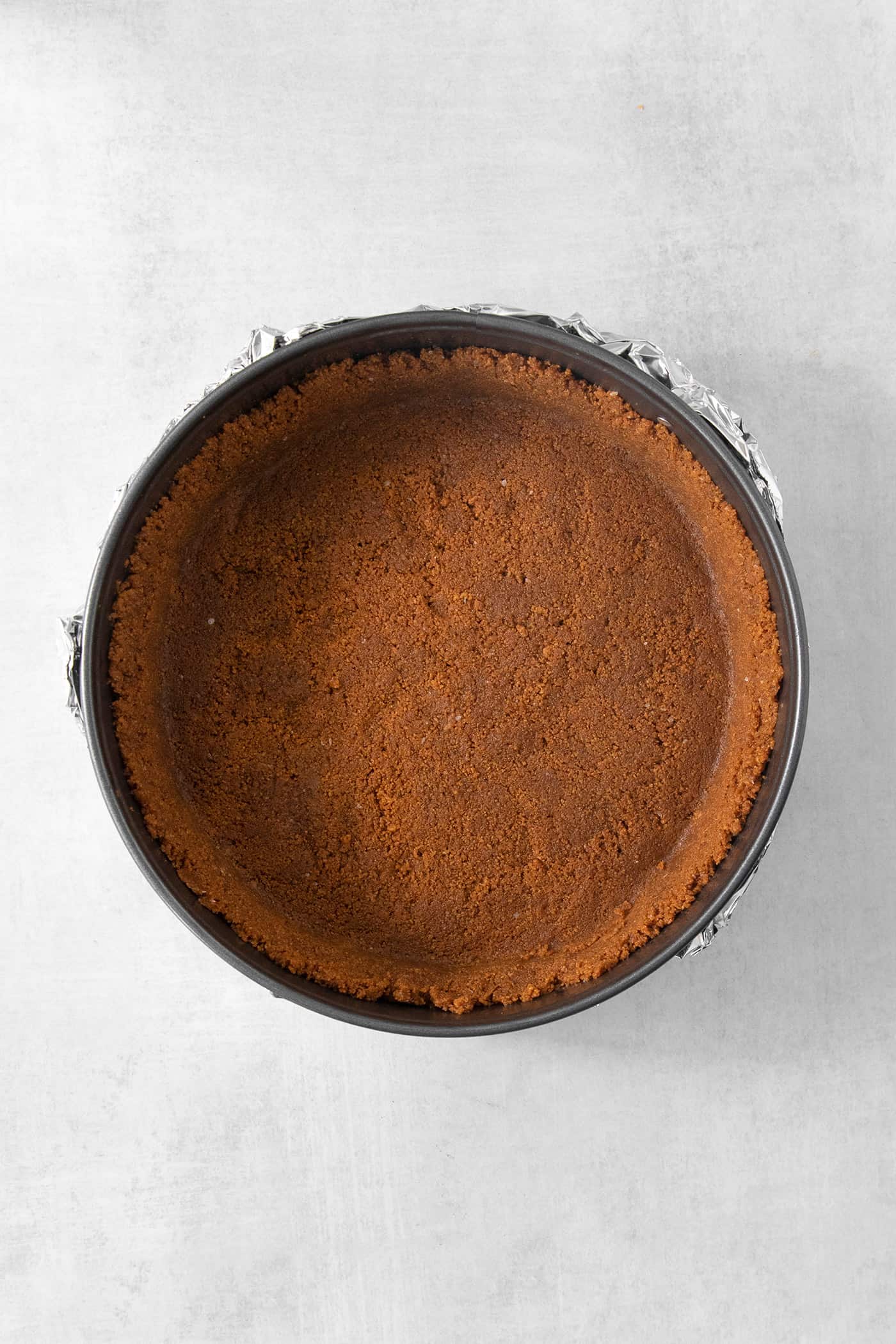 This Biscoff Cheesecake balances a rich cream cheese layer swirled with Biscoff cookie butter on a buttery cookie crust. A biscoff cookie crust is shown in a springform pan.
