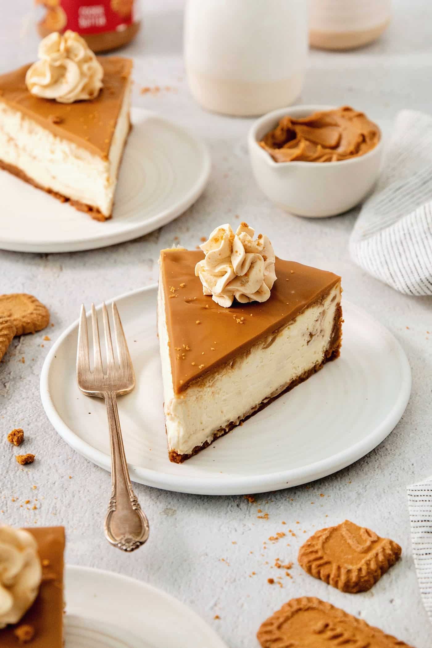 This Biscoff Cheesecake balances a rich cream cheese layer swirled with Biscoff cookie butter on a buttery cookie crust. A slice of biscoff cheesecake is shown on a plate with biscoff cookie butter in the background.