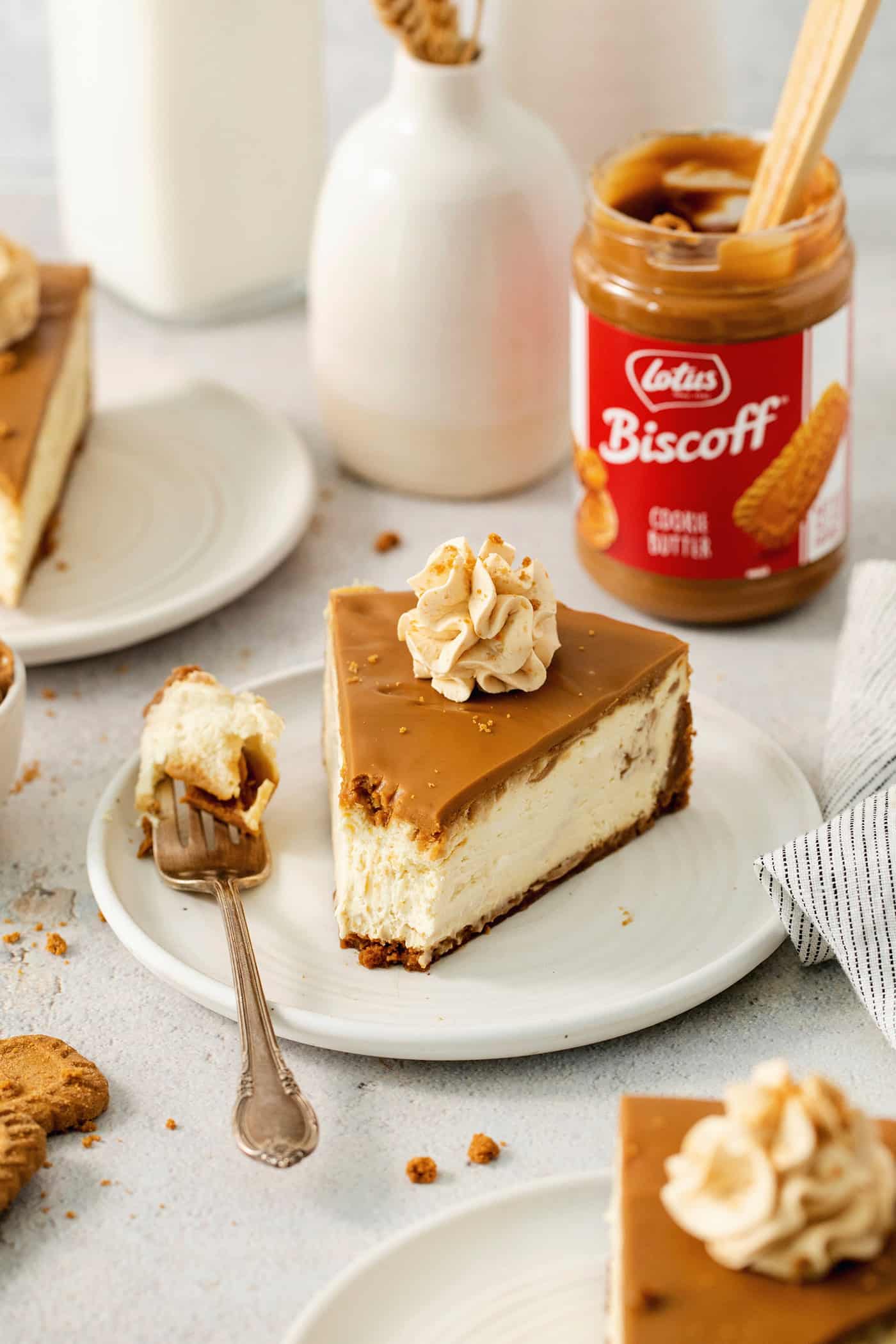 This Biscoff Cheesecake balances a rich cream cheese layer swirled with Biscoff cookie butter on a buttery cookie crust. A slice of biscoff cheesecake is shown on a plate with biscoff cookie butter in the background.