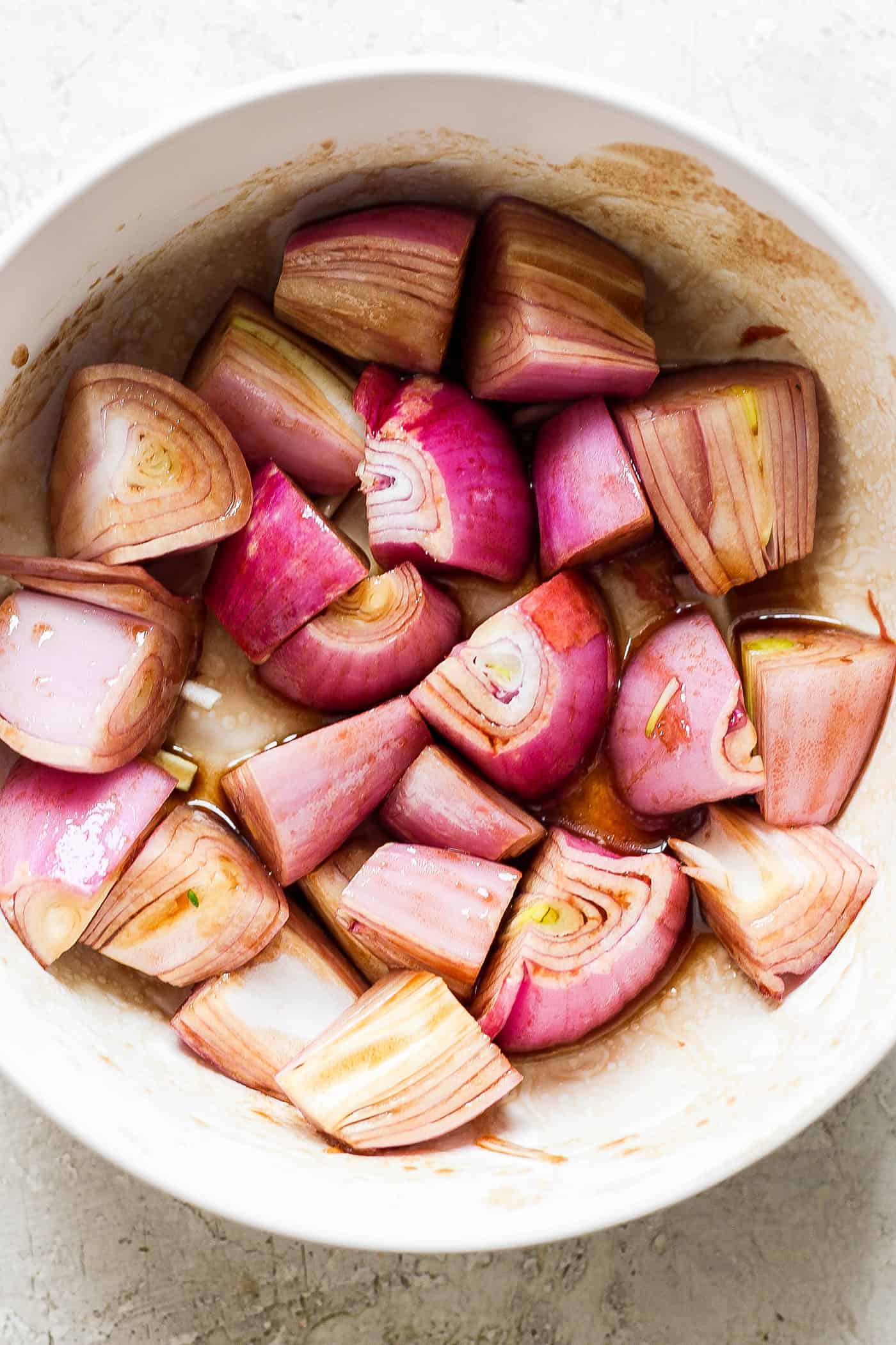 These tender Chicken Kabobs with Rapes are marinated in a lemon yogurt sauce and paired with honey balsamic shallots and sweet juicy grapes. Shallots are shown marinating in a white bowl.