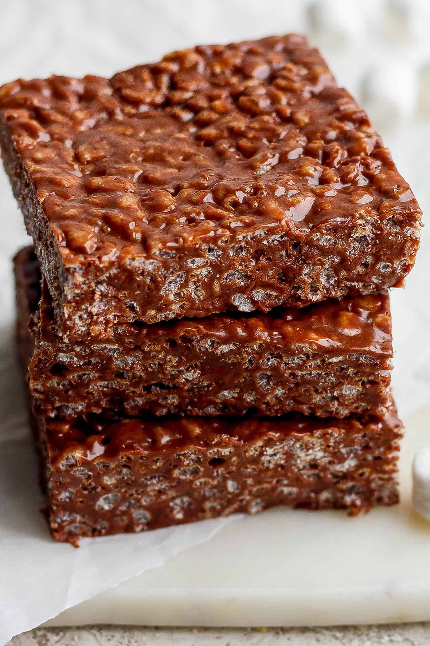 Chocolate Rice Krispie Treats have a chewy, fudge-like texture and are full of rich chocolate and sweet marshmallow flavor. A stack of 3 chocolate rice krispie treats on a white board.