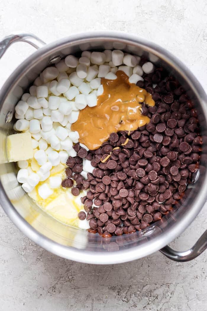 Chocolate Rice Krispie Treats have a chewy, fudge-like texture and are full of rich chocolate and sweet marshmallow flavor. Mini marshmallows, chocolate chips, butter, and peanut butter are shown in a pot.