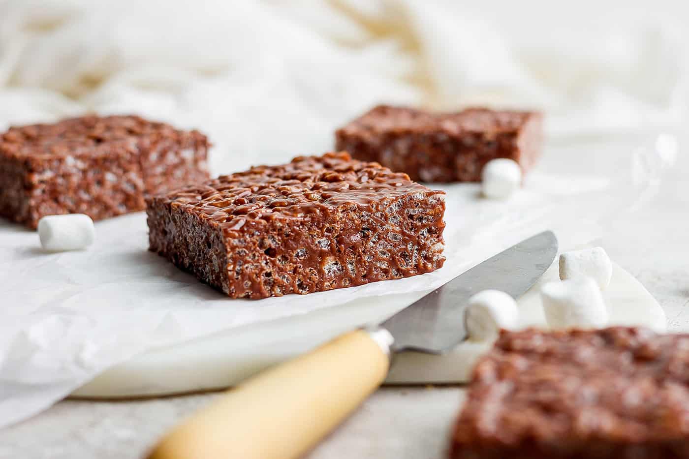 Chocolate Rice Krispie Treats have a chewy, fudge-like texture and are full of rich chocolate and sweet marshmallow flavor. Chocolate rice krispie treats are shown on a white cutting board.