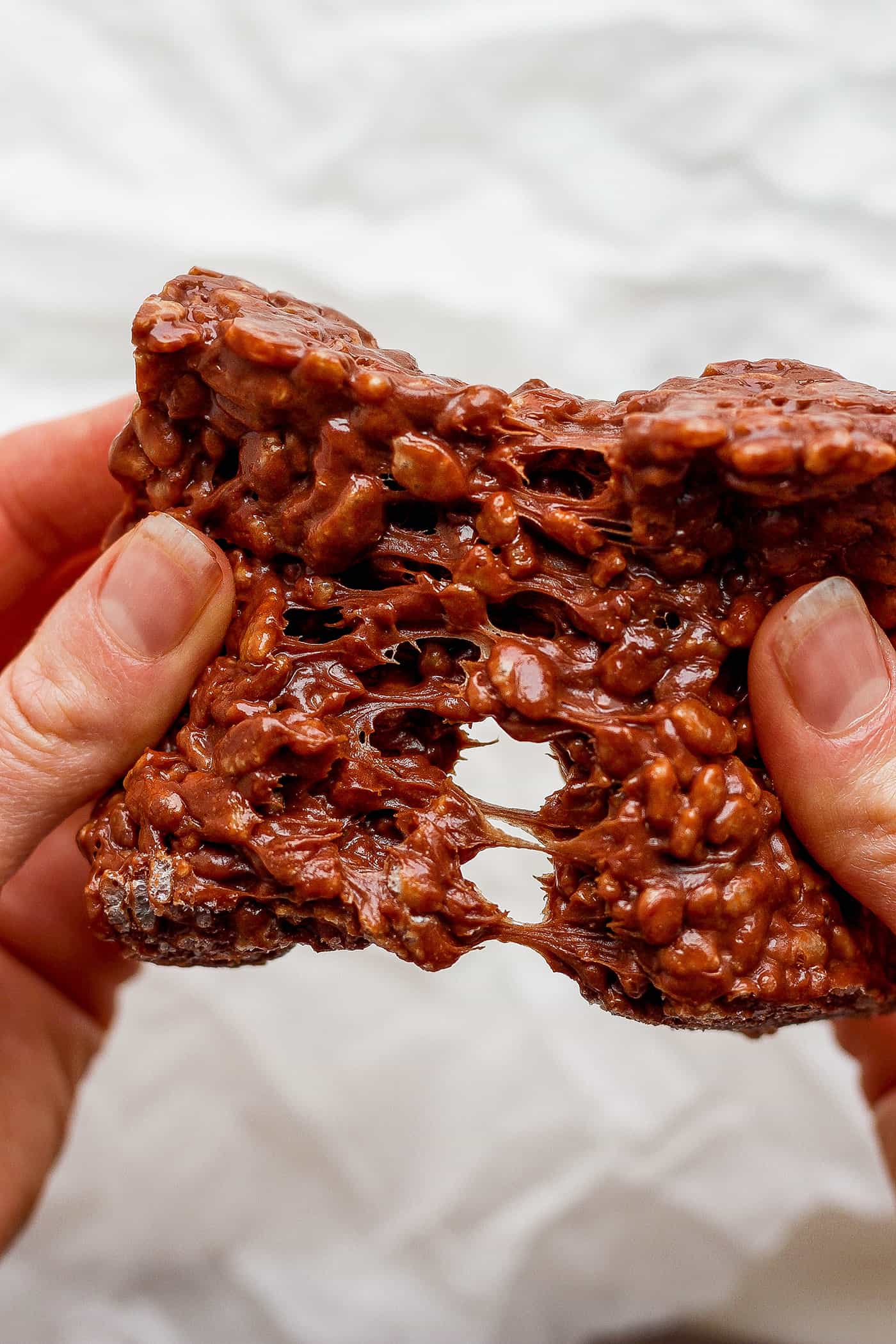 Chocolate Rice Krispie Treats have a chewy, fudge-like texture and are full of rich chocolate and sweet marshmallow flavor. A hand pulls apart a chocolate rice krispie treat.