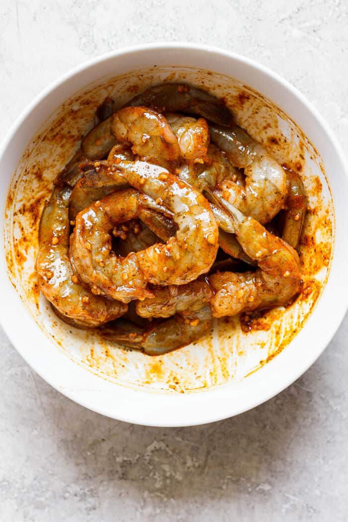 Juicy, flavorful Grilled Shrimp is ready in just minutes! Tender shrimp is bathed in an easy, sweet-smoky marinade and served with lemon. A white bowl of shrimp in a spicy marinade.