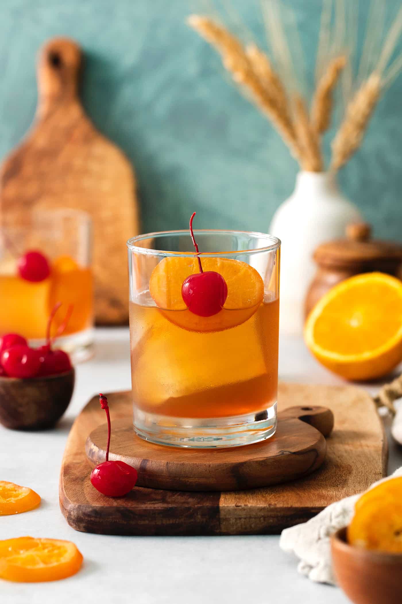 This classic Old Fashioned is a go-to before-dinner cocktail! It’s simple and easy, made with just three ingredients: whiskey, simple syrup, and bitters. An old fashioned drink is shown on a wood board with more drinks and oranges in the background.