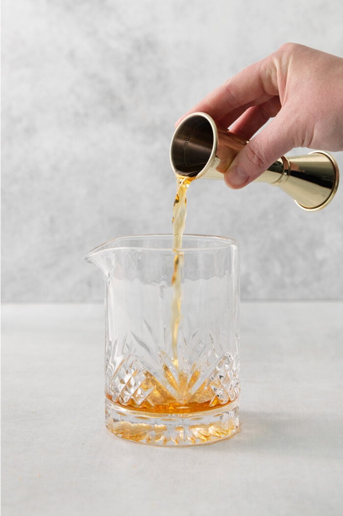 This classic Old Fashioned is a go-to before-dinner cocktail! It’s simple and easy, made with just three ingredients: whiskey, simple syrup, and bitters. A hand holds a cocktail measure and pours bourbon into a glass of old fashioned.