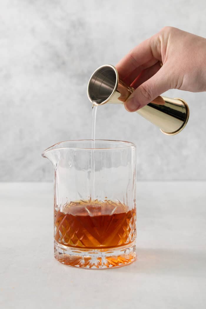 This classic Old Fashioned is a go-to before-dinner cocktail! It’s simple and easy, made with just three ingredients: whiskey, simple syrup, and bitters. A hand holds a cocktail measure and pours simple syrup into a glass of old fashioned.