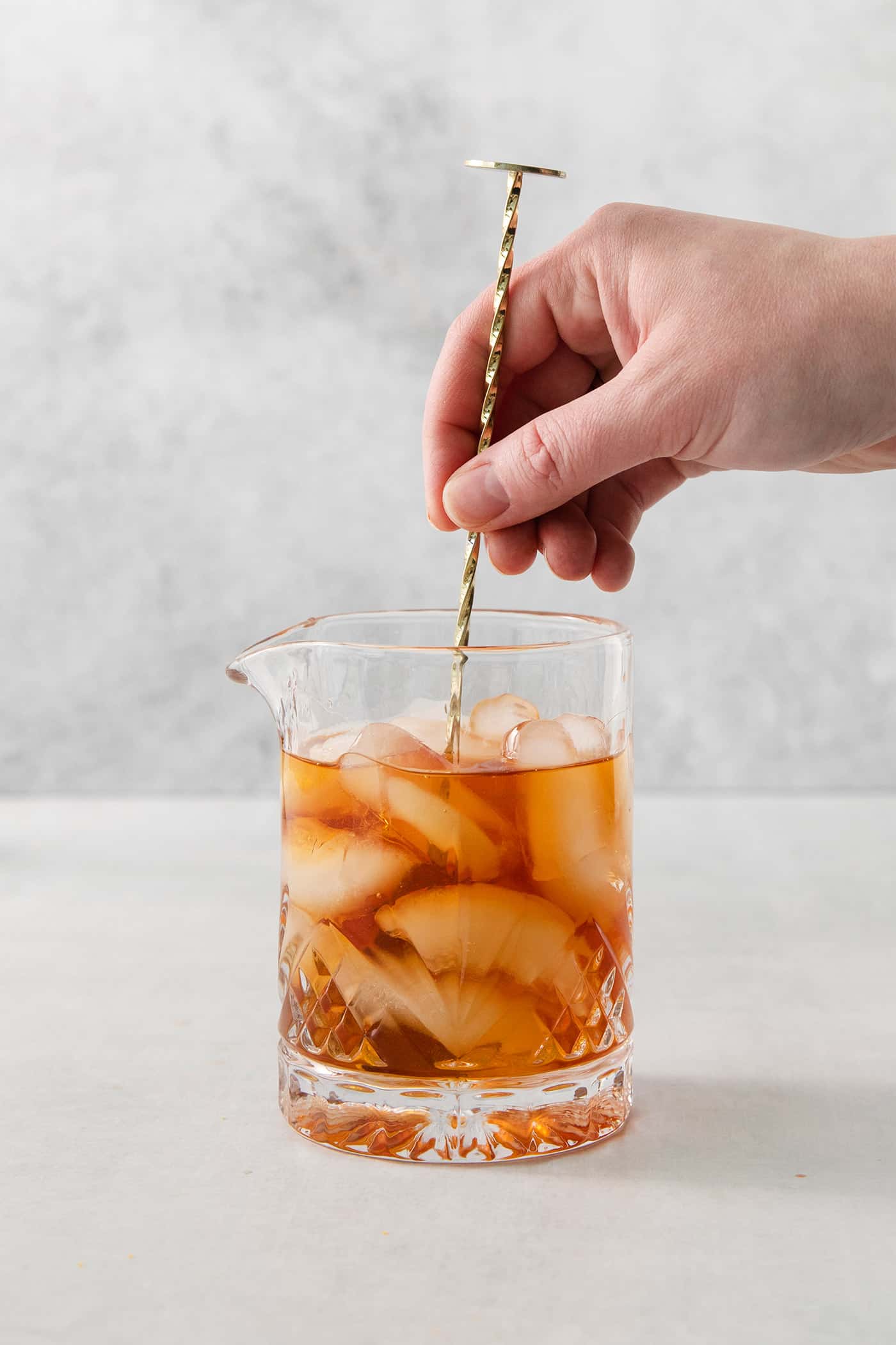 This classic Old Fashioned is a go-to before-dinner cocktail! It’s simple and easy, made with just three ingredients: whiskey, simple syrup, and bitters. A hand holds a stirrer and stirs a glass of old fashioned.