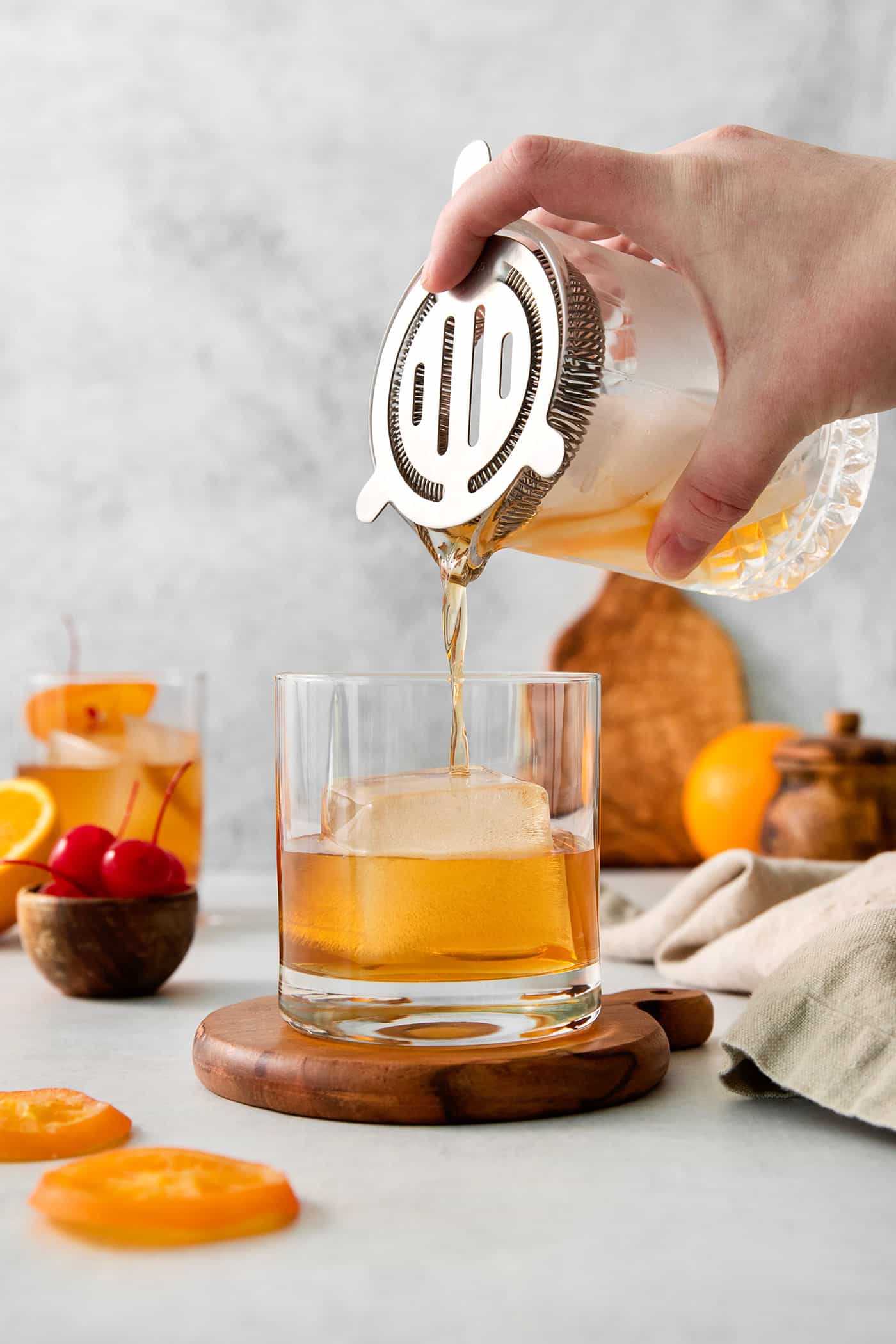 This classic Old Fashioned is a go-to before-dinner cocktail! It’s simple and easy, made with just three ingredients: whiskey, simple syrup, and bitters. A hand holds a cocktail shaker and pours an old fashioned drink into a glass.