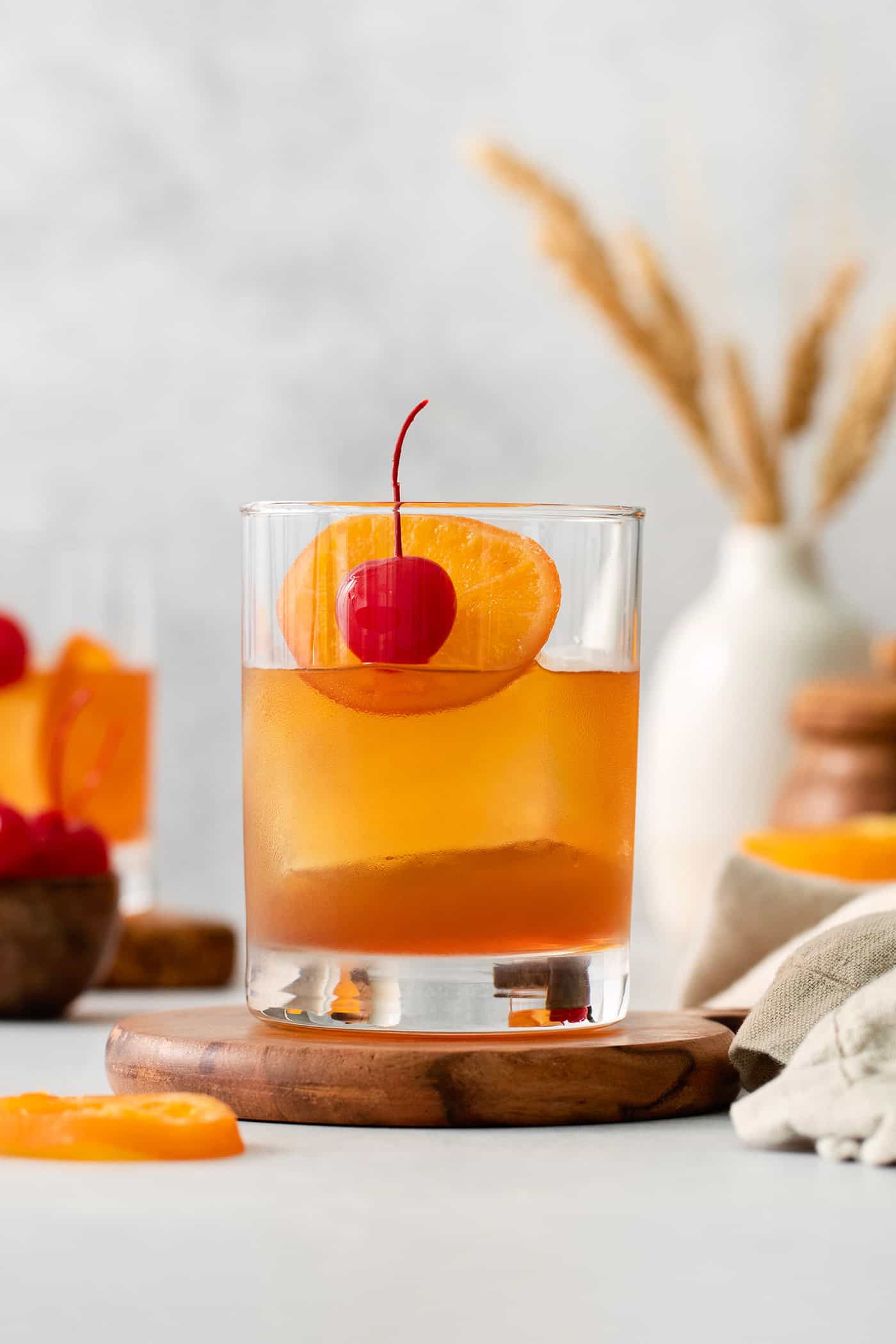 This classic Old Fashioned is a go-to before-dinner cocktail! It’s simple and easy, made with just three ingredients: whiskey, simple syrup, and bitters. An old fashioned drink is shown on a wood board with more drinks and oranges in the background.