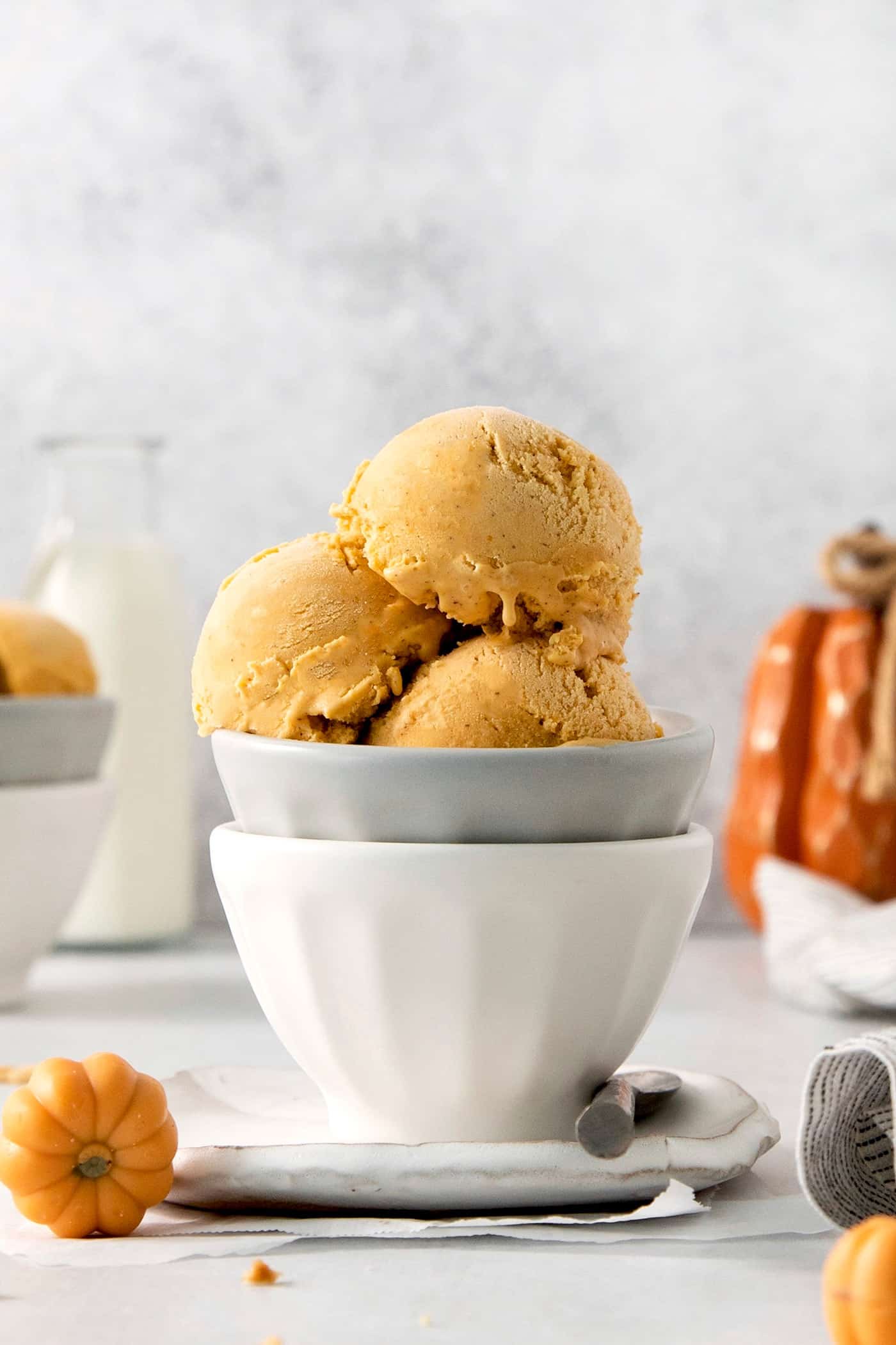 This Pumpkin Ice Cream is rich and creamy, flavored with pumpkin puree and pumpkin pie spice, and sweetened with brown sugar. Three scoops of orange pumpkin ice cream are shown in a gray bowl stacked in a white bowl.