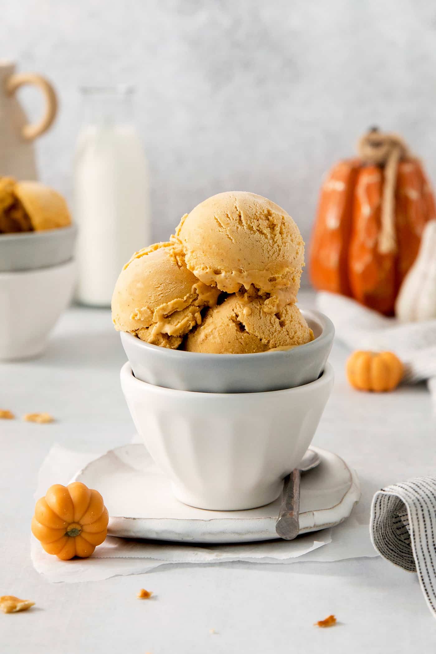 This Pumpkin Ice Cream is rich and creamy, flavored with pumpkin puree and pumpkin pie spice, and sweetened with brown sugar. Custard-based ice creams may seem intimidating, but this one is very easy and only requires a handful of ingredients. Three scoops of orange pumpkin ice cream are shown in a gray bowl stacked in a white bowl.