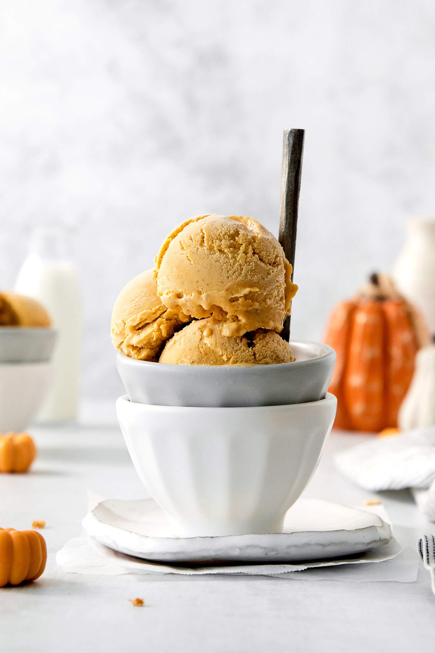 This Pumpkin Ice Cream is rich and creamy, flavored with pumpkin puree and pumpkin pie spice, and sweetened with brown sugar. Three scoops of orange pumpkin ice cream are shown in a gray bowl stacked in a white bowl.