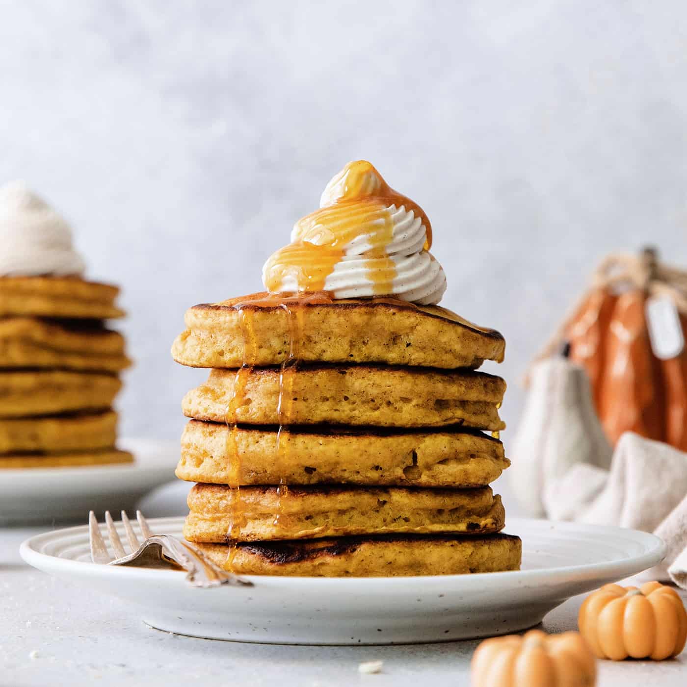 These Pumpkin Pancakes are rich and fluffy, flavored with buttermilk, pumpkin puree, and pumpkin pie spice for the perfect fall breakfast! A stack of pumpkin pancakes topped with maple cinnamon whipped cream on a white plate.