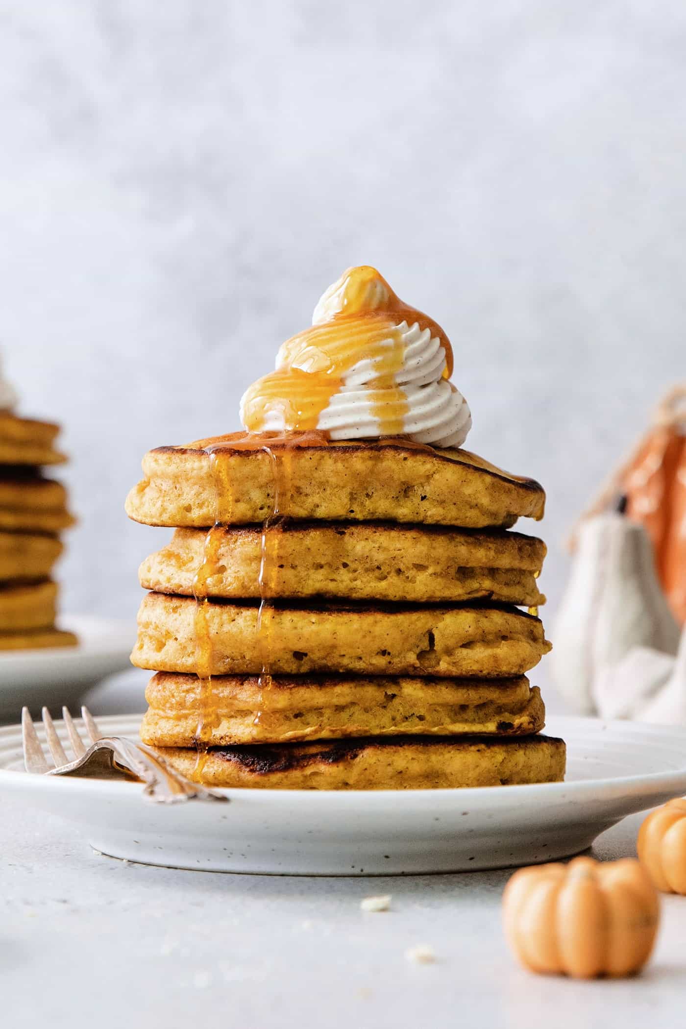 These Pumpkin Pancakes are rich and fluffy, flavored with buttermilk, pumpkin puree, and pumpkin pie spice for the perfect fall breakfast! A stack of pumpkin pancakes topped with maple cinnamon whipped cream on a white plate.