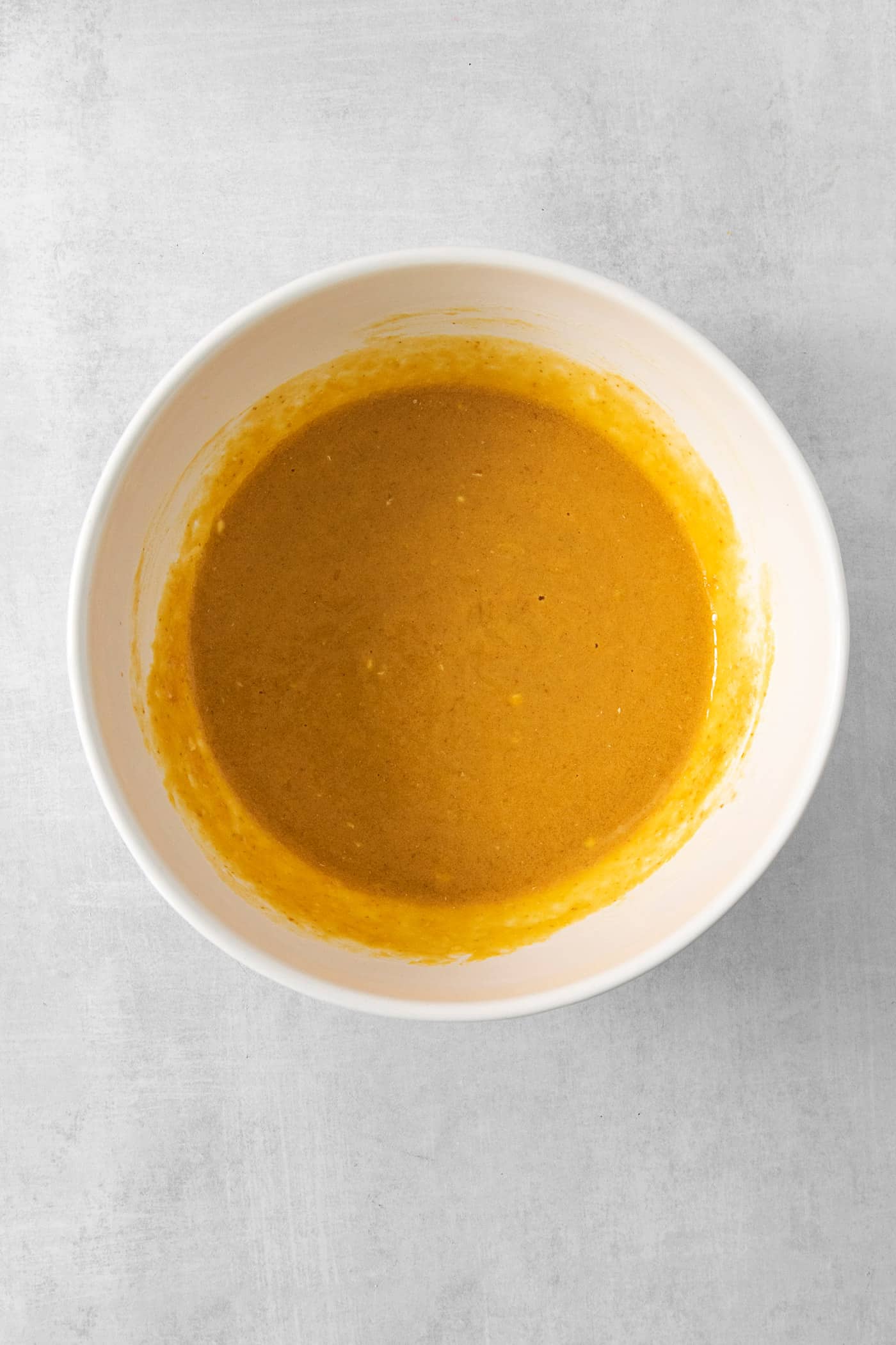 These Pumpkin Pancakes are rich and fluffy, flavored with buttermilk, pumpkin puree, and pumpkin pie spice for the perfect fall breakfast! Pumpkin puree is mixed with other ingedients in a white bowl to make pumpkin pancakes.