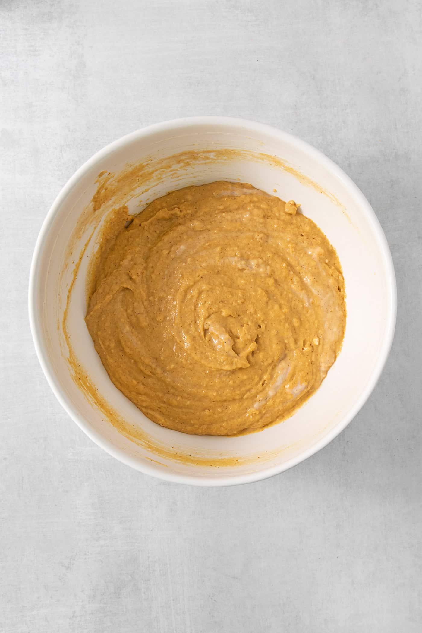 These Pumpkin Pancakes are rich and fluffy, flavored with buttermilk, pumpkin puree, and pumpkin pie spice for the perfect fall breakfast! A white bowl full of pumpkin pancakes batter is shown on a white background.