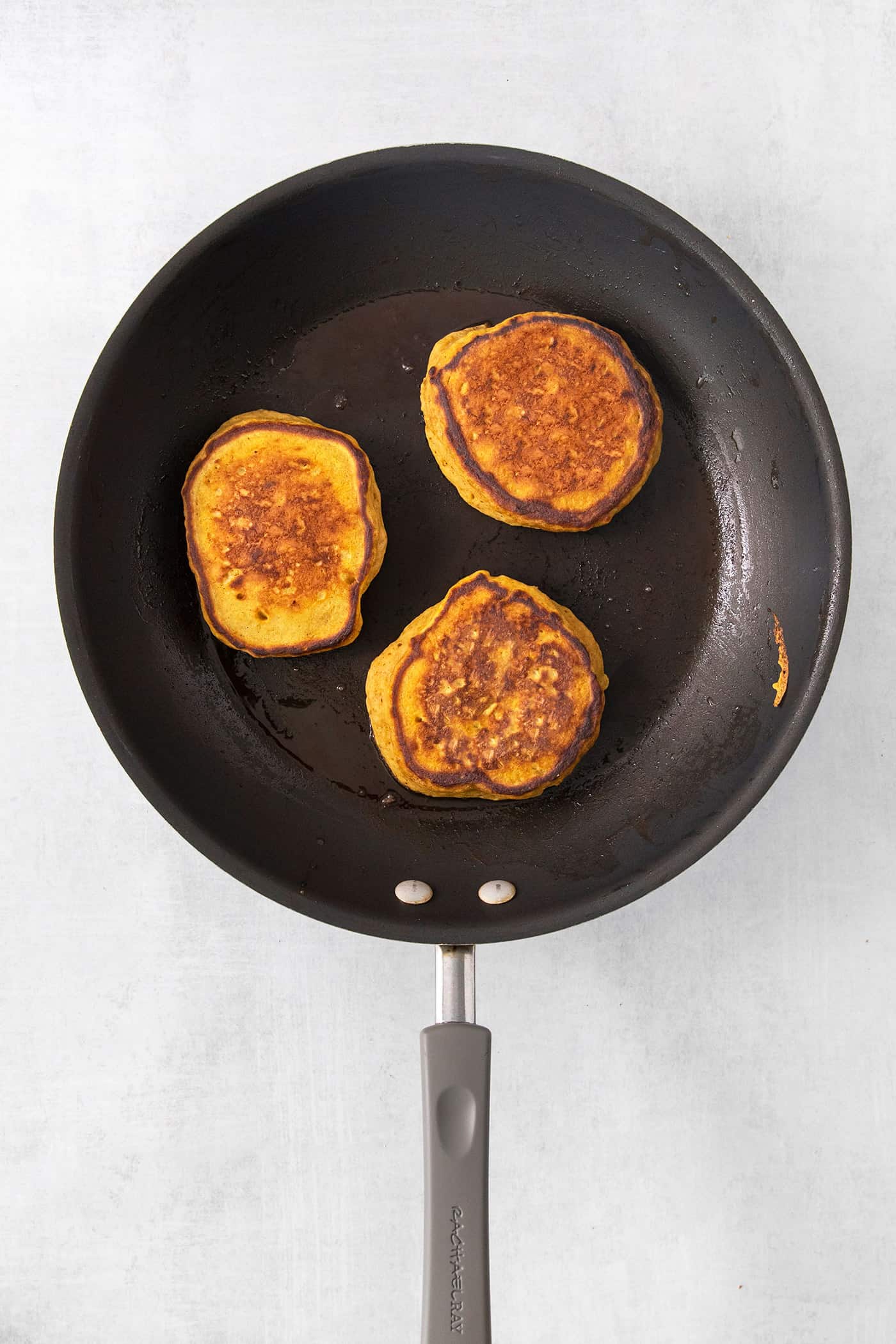 These Pumpkin Pancakes are rich and fluffy, flavored with buttermilk, pumpkin puree, and pumpkin pie spice for the perfect fall breakfast! Three pumpkin pancakes cook in a frying pan.