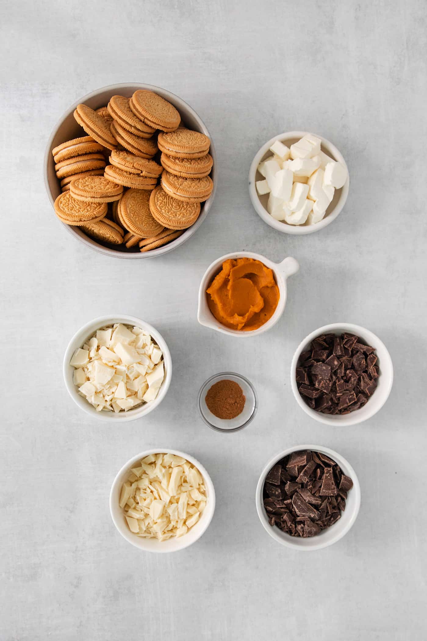 These Pumpkin Pie Truffles are the perfect fall treat! The truffle filling is made with crisp cookies, cream cheese, pumpkin puree, and spice. Ingredients for pumpkin pie truffles are shown in bowls: golden Oreos, pumpkin puree, sugar, spices, and cream cheese.