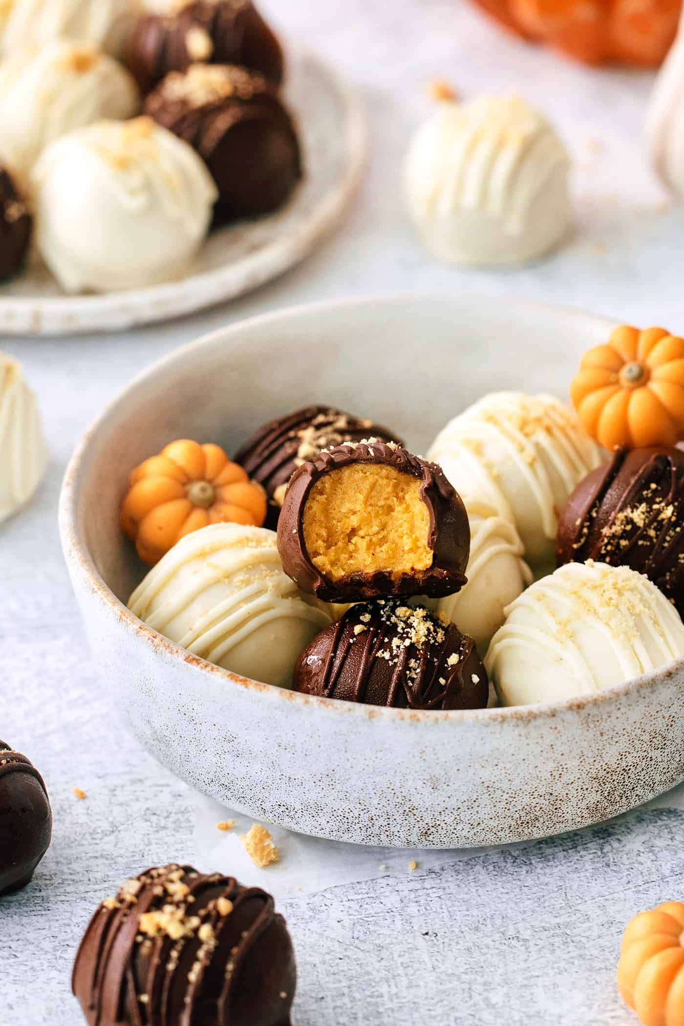 These Pumpkin Pie Truffles are the perfect fall treat! The truffle filling is made with crisp cookies, cream cheese, pumpkin puree, and spice. A white bowl of pumpkin pie truffles is shown on a white background.