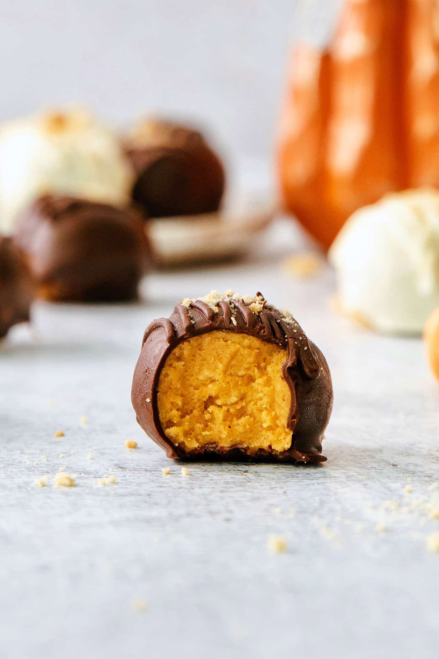 These Pumpkin Pie Truffles are the perfect fall treat! The truffle filling is made with crisp cookies, cream cheese, pumpkin puree, and spice. A chocolate covered pumpkin pie truffle is shown with a bite taken out of it.