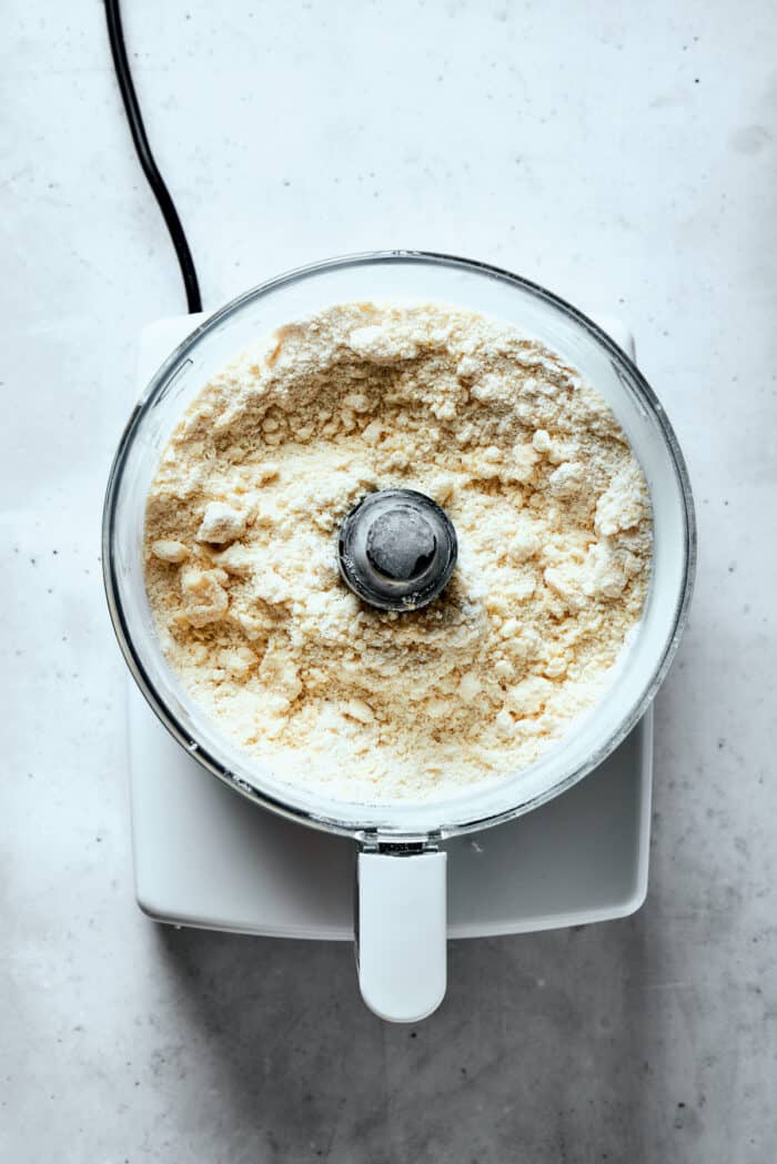 Napoleon Cake takes flaky homemade pastry and layers it with a sumptuous egg custard to make a creamy and cool dessert! A crumbly pastry dough mix is shown in a food processor.