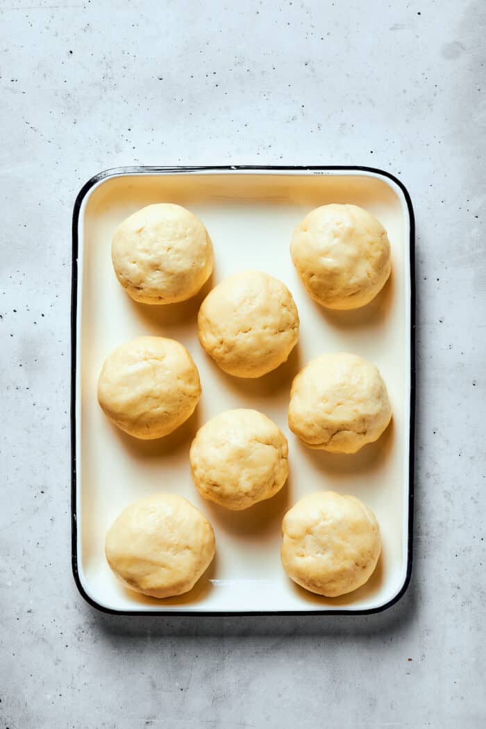 Napoleon Cake takes flaky homemade pastry and layers it with a sumptuous egg custard to make a creamy and cool dessert! Eight balls of pastry dough are shown on a rimmed baking sheet.