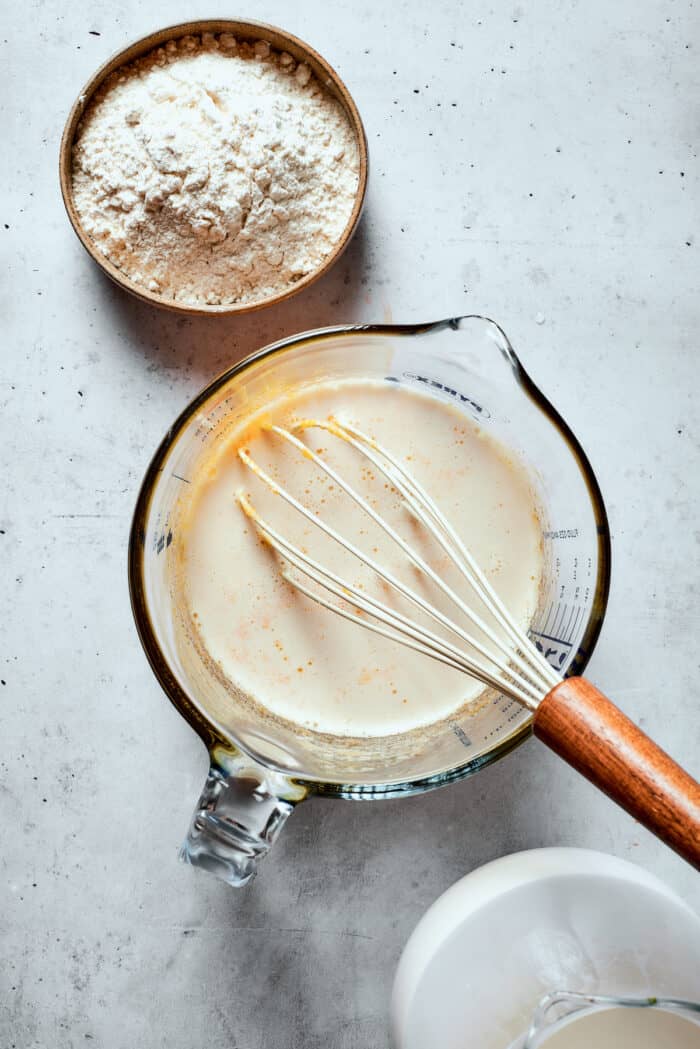 Napoleon Cake takes flaky homemade pastry and layers it with a sumptuous egg custard to make a creamy and cool dessert! A glass cup full of pastry cream mix and a whisk.