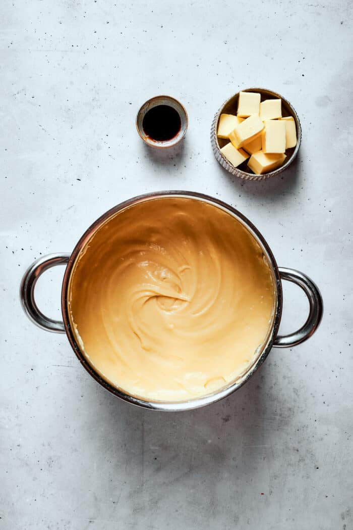 Napoleon Cake takes flaky homemade pastry and layers it with a sumptuous egg custard to make a creamy and cool dessert! A top down shot of pastry cream with a bowl of cubed butter on the side.