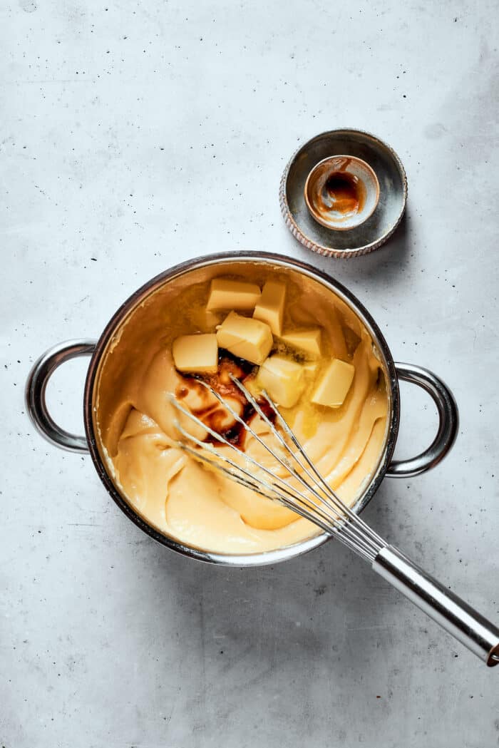 Napoleon Cake takes flaky homemade pastry and layers it with a sumptuous egg custard to make a creamy and cool dessert! Butter is whisked into a pot of pastry cream.