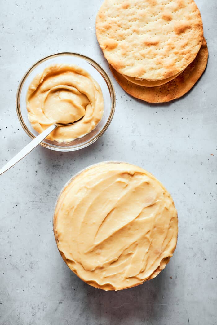 Napoleon Cake takes flaky homemade pastry and layers it with a sumptuous egg custard to make a creamy and cool dessert! A bowl of pastry cream next to a Napoleon cake and a stack of pastry rounds.