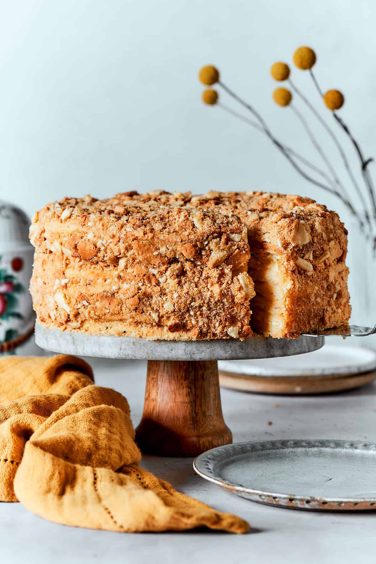 Napoleon Cake takes flaky homemade pastry and layers it with a sumptuous egg custard to make a creamy and cool dessert! A Napoleon cake is shown on a cake stand.