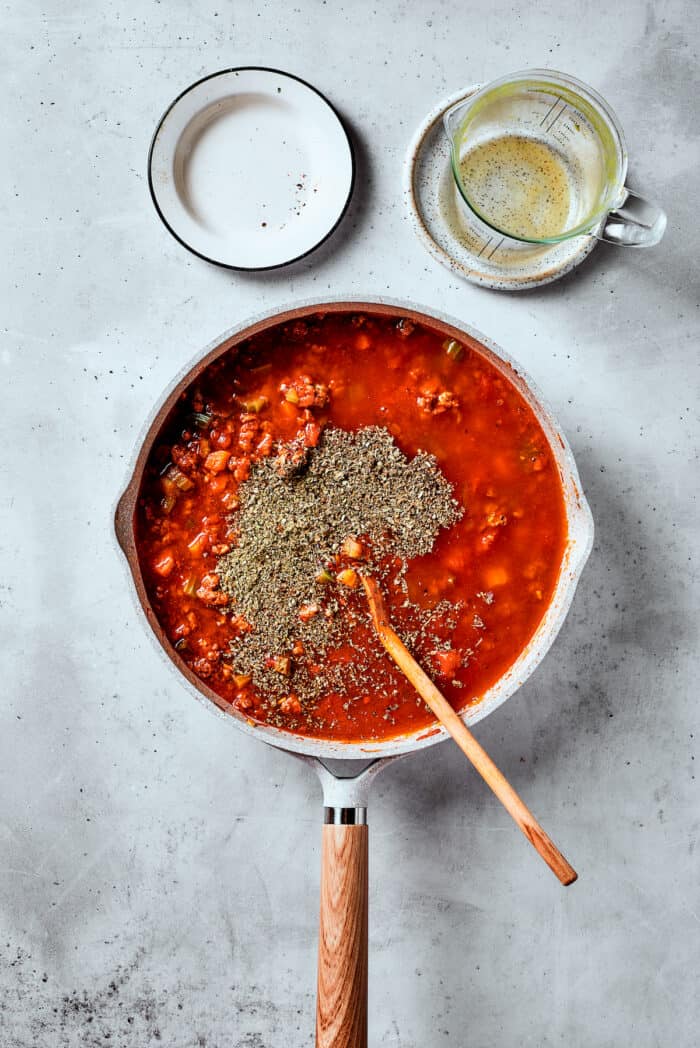 Easy, Italian-inspired Pasta Fazool is a wonderful soup that pairs creamy white beans with ground meat and pasta in a tomato-based broth. Herbs are shown on top of a pot of pasta fazool.