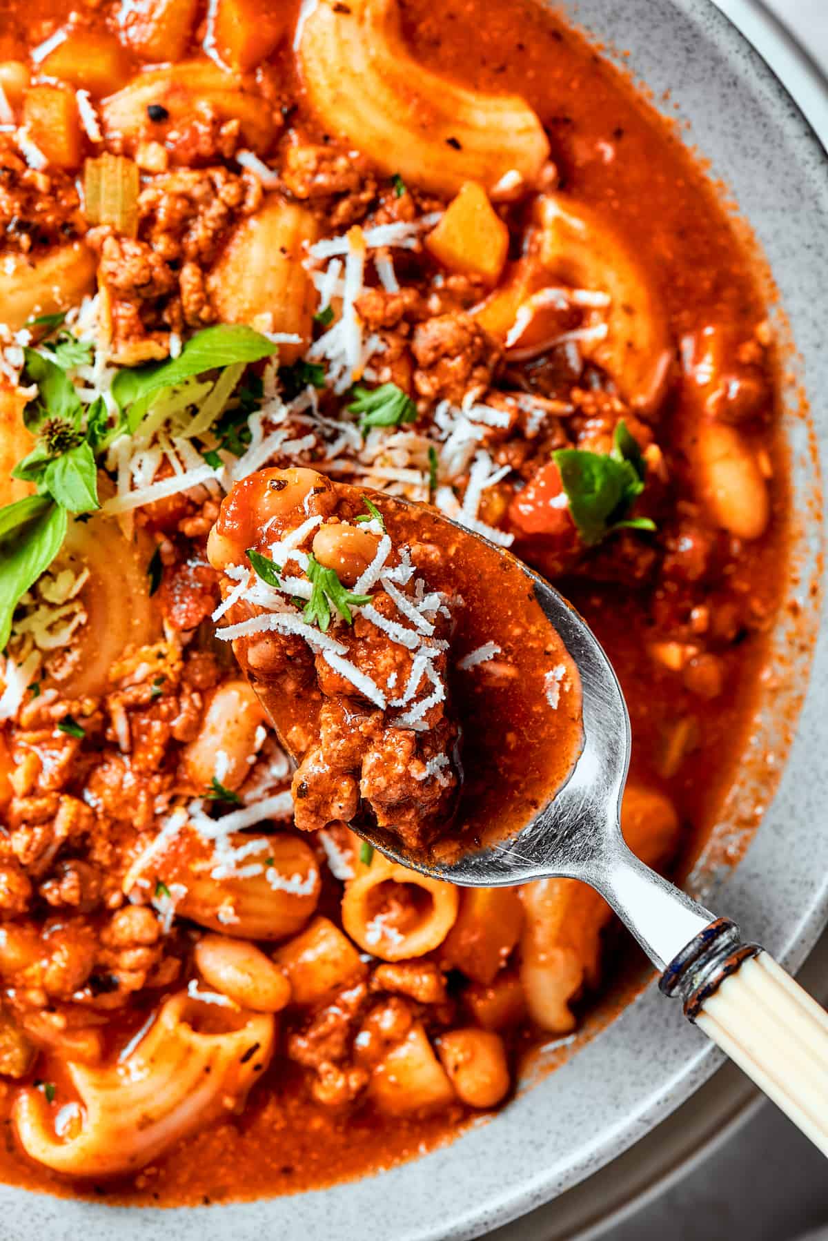 Easy, Italian-inspired Pasta Fazool is a wonderful soup that pairs creamy white beans with ground meat and pasta in a tomato-based broth. A spoon holds pasta fazool over a bowl.