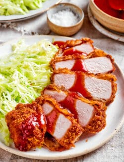 sliced pork katsu with sauce drizzled over the top, on a white plate