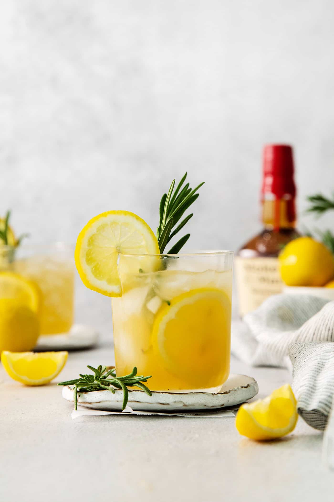 This Bourbon Limoncello Cocktail is a refreshing drink featuring fresh rosemary, lemon, honey, bourbon, and limoncello. A glass of bourbon limoncello cocktail garnished with a lemon wheel and a sprig of fresh rosemary.