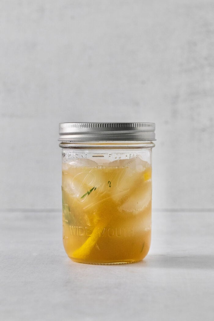 This Bourbon Limoncello Cocktail is a refreshing drink featuring fresh rosemary, lemon, honey, bourbon, and limoncello. A glass jar with a lid holds bourbon limoncello cocktail.