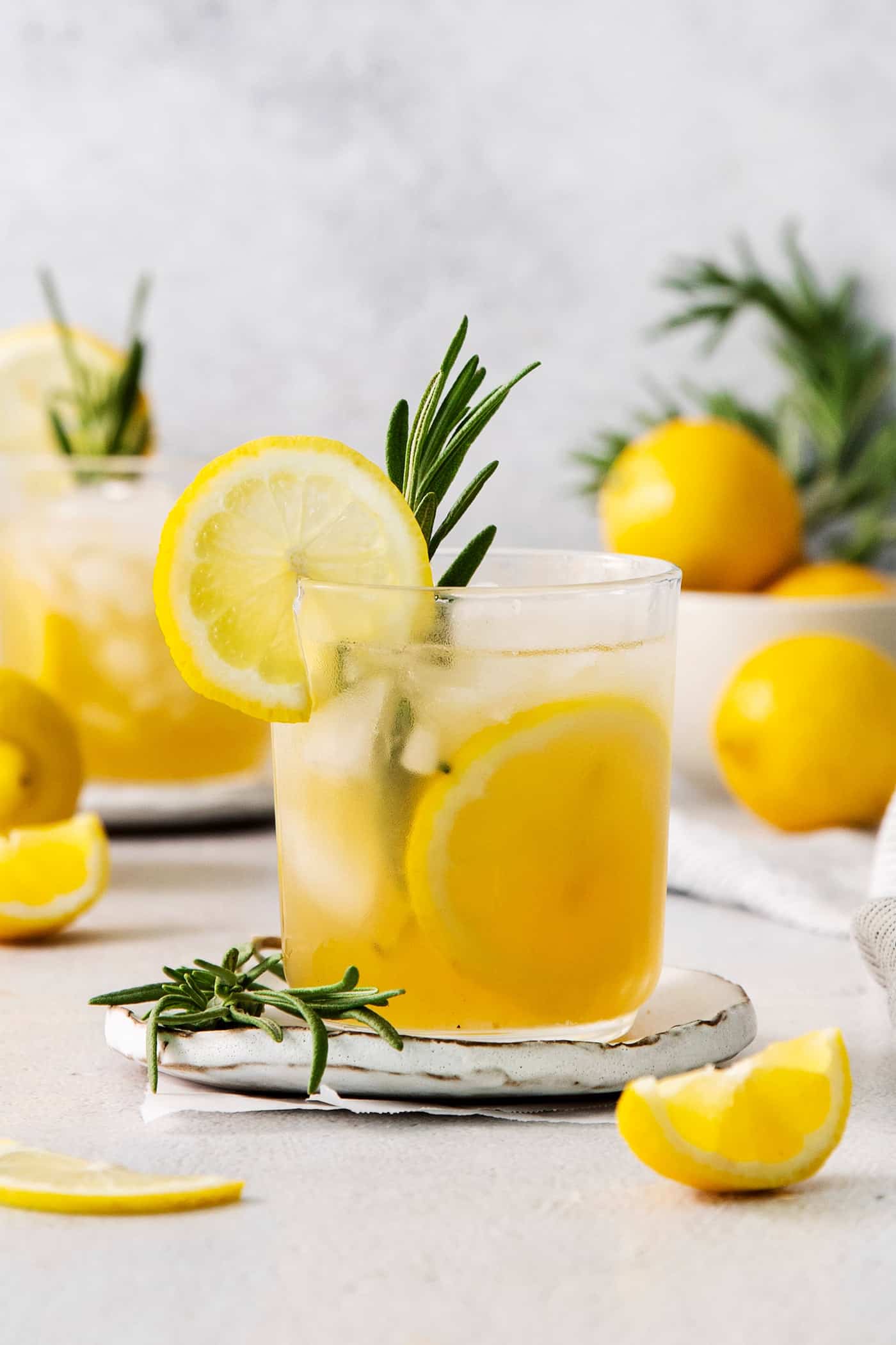 This Bourbon Limoncello Cocktail is a refreshing drink featuring fresh rosemary, lemon, honey, bourbon, and limoncello. A glass of bourbon limoncello cocktail garnished with a lemon wheel and a sprig of fresh rosemary.