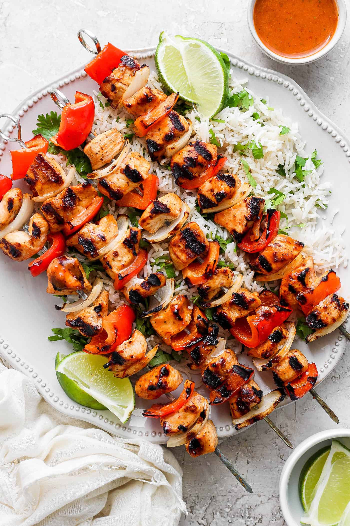 Sweet-spicy Chipotle Honey Chicken Kabobs bathe tender chicken in a honey-infused vinaigrette with a kick of spice. A platter of chipotle honey chicken kabobs is shown with lime wedges.