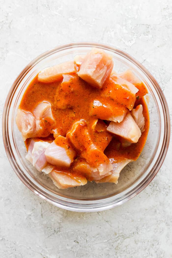 Sweet-spicy Chipotle Honey Chicken Kabobs bathe tender chicken in a honey-infused vinaigrette with a kick of spice. Chicken and vegetables marinate in a glass bowl.