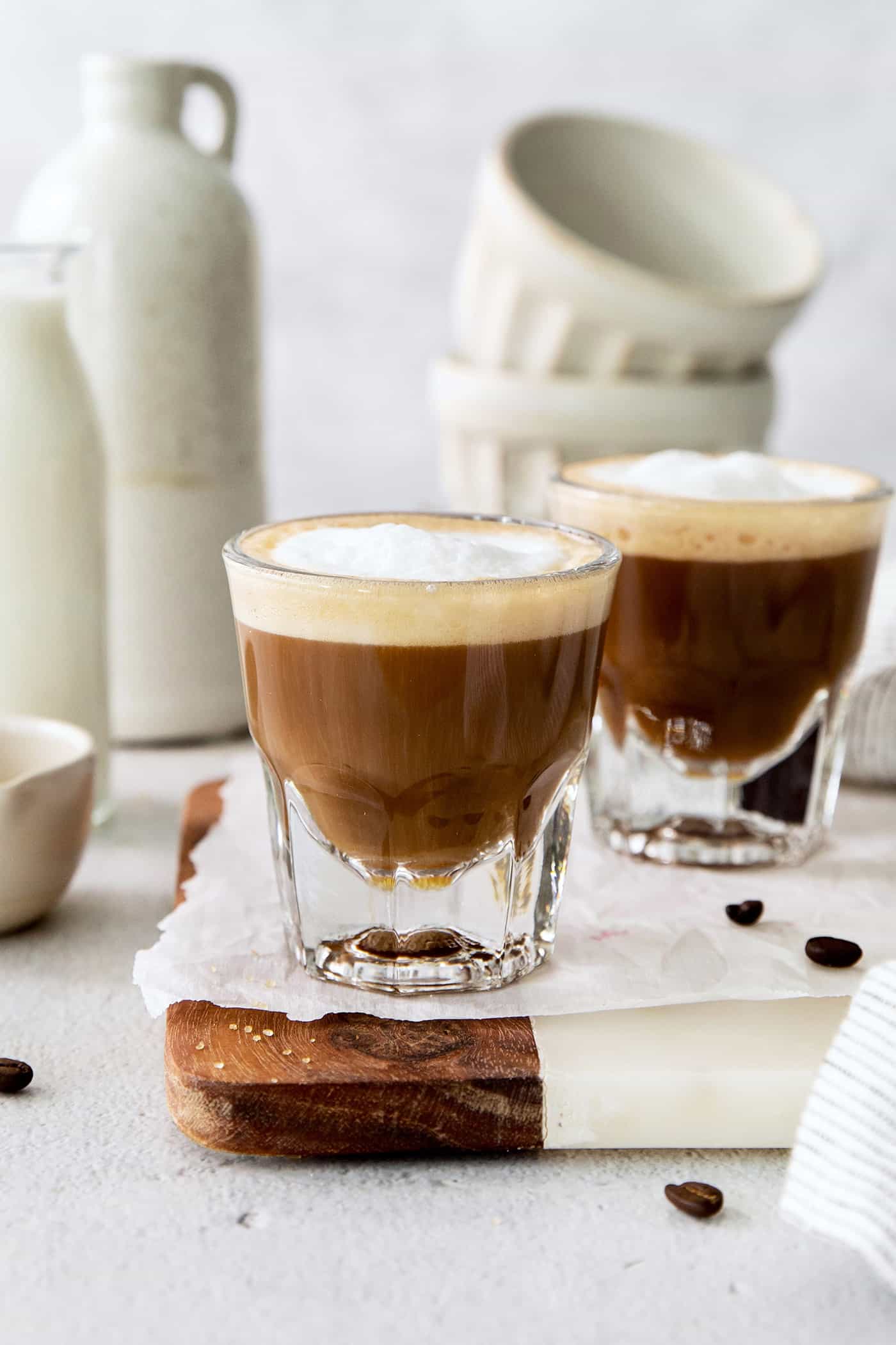 A Cortadito is a classic Cuban coffee made from equal parts sweetened espresso and frothed milk. It is rich, creamy, and sweet. Two cortaditos are shown on a board with milk in the background.