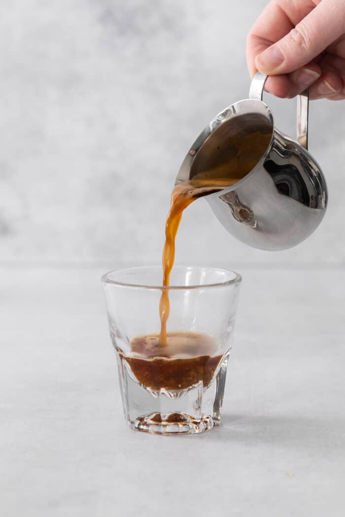 A Cortadito is a classic Cuban coffee made from equal parts sweetened espresso and frothed milk. It is rich, creamy, and sweet. A hand pours a pitcher of espresso into a small glass.