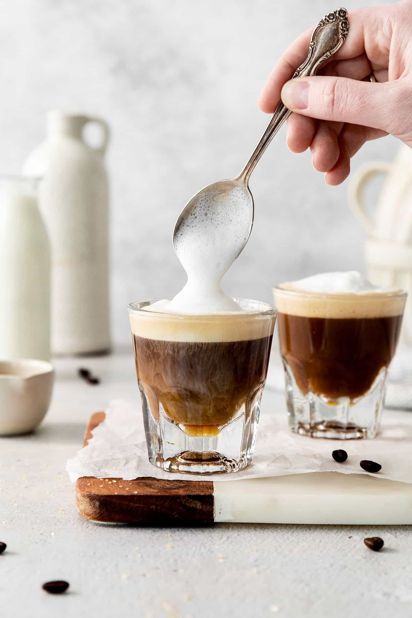 A Cortadito is a classic Cuban coffee made from equal parts sweetened espresso and frothed milk. It is rich, creamy, and sweet. A hand holding a spoon tops cortaditos with frothed milk.