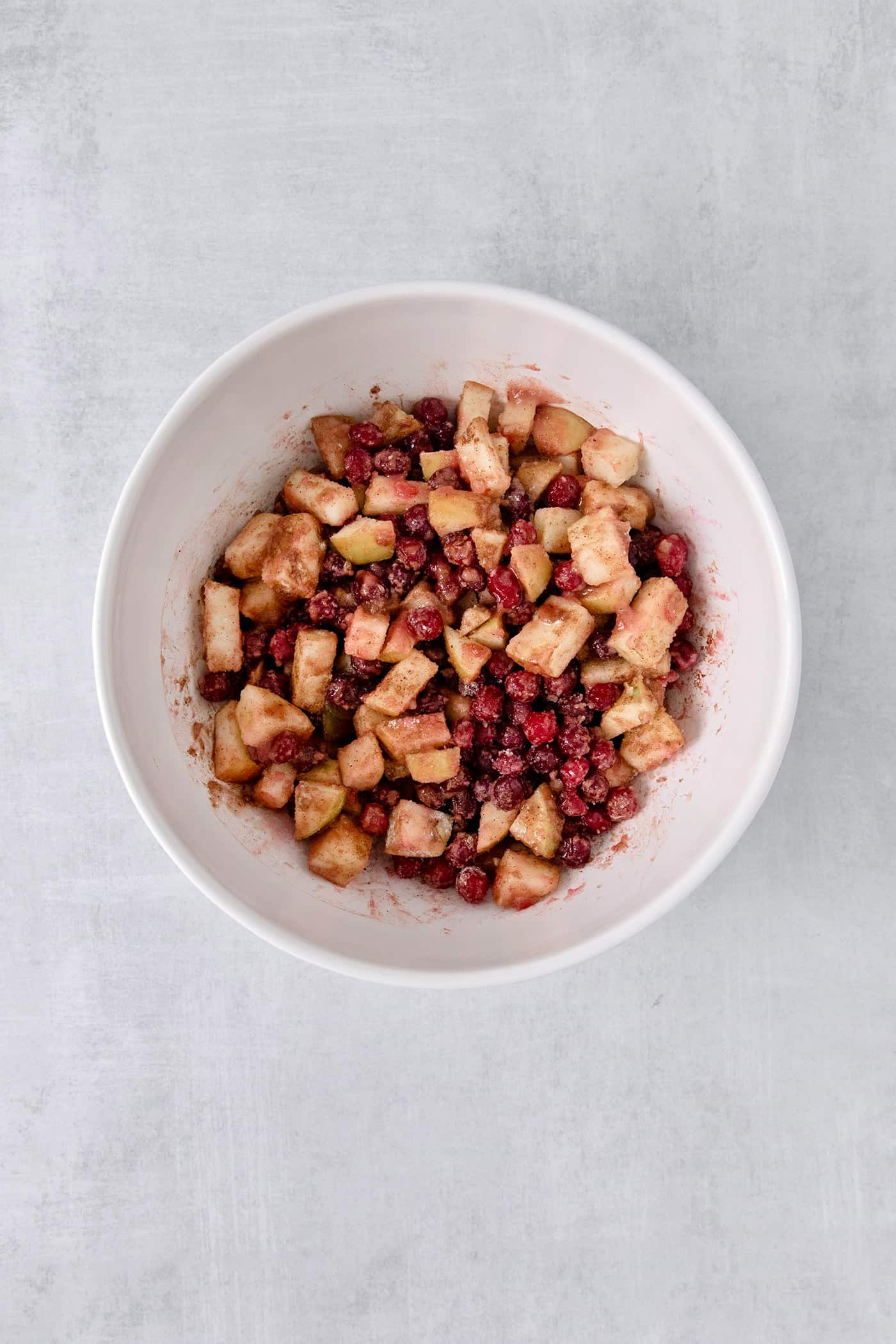 This Cranberry Apple Crisp features fresh, sweet-tart cranberries and apples, plus a crispy, buttery oat topping. A white bowl of cranberry apple crisp filling.