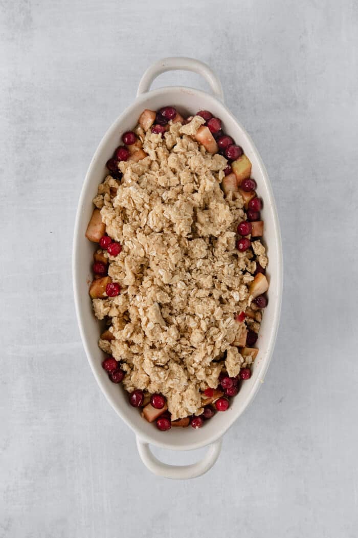 This Cranberry Apple Crisp features fresh, sweet-tart cranberries and apples, plus a crispy, buttery oat topping. A white oval baking dish holds a baked cranberry apple crisp.